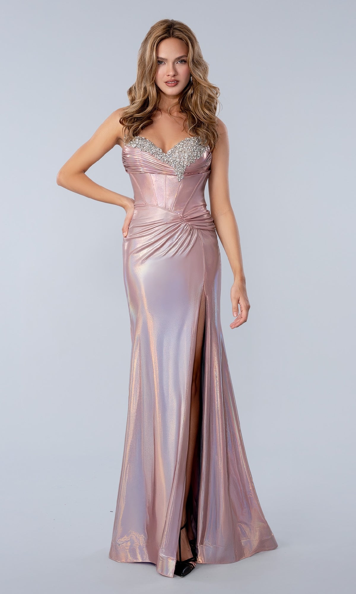 A woman poses against a plain light background in the Stella Couture 26200 long prom dress in rose, featuring a shiny, form-fitting metallic style with a sweetheart neckline, jeweled corset bodice, ruched waist, and thigh-high slit.